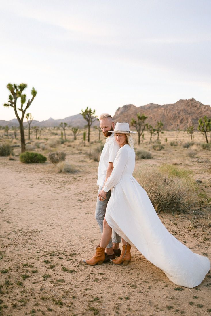 A tender moment captured in the desert with mountains and Joshua trees.