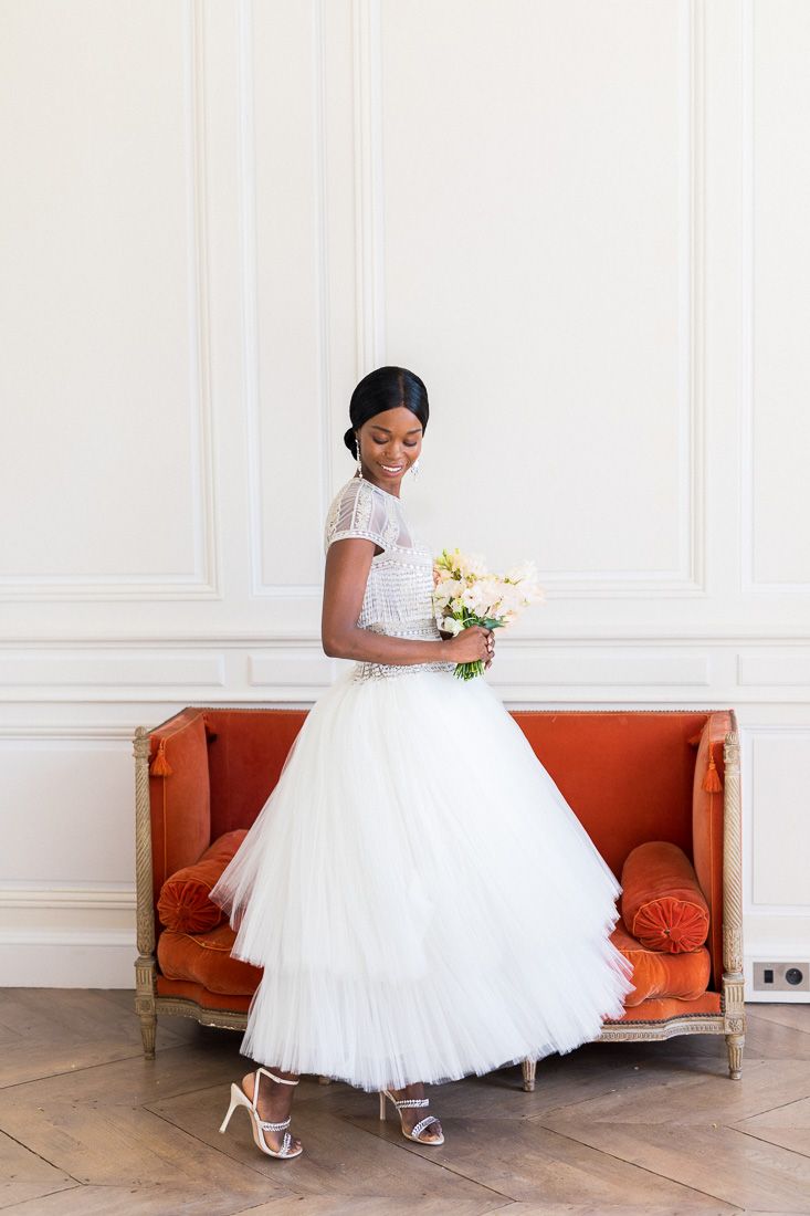 Joyful bridal portrait in a tea-length tulle gown against white paneled walls.