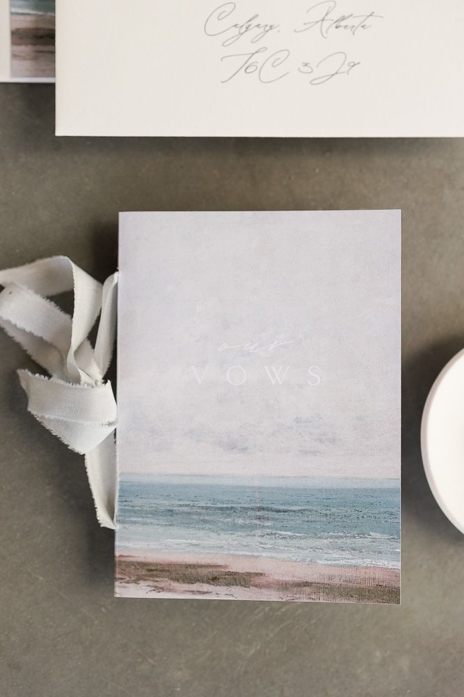 A minimalist wedding invitation featuring a serene coastal beach scene in soft pastel tones.