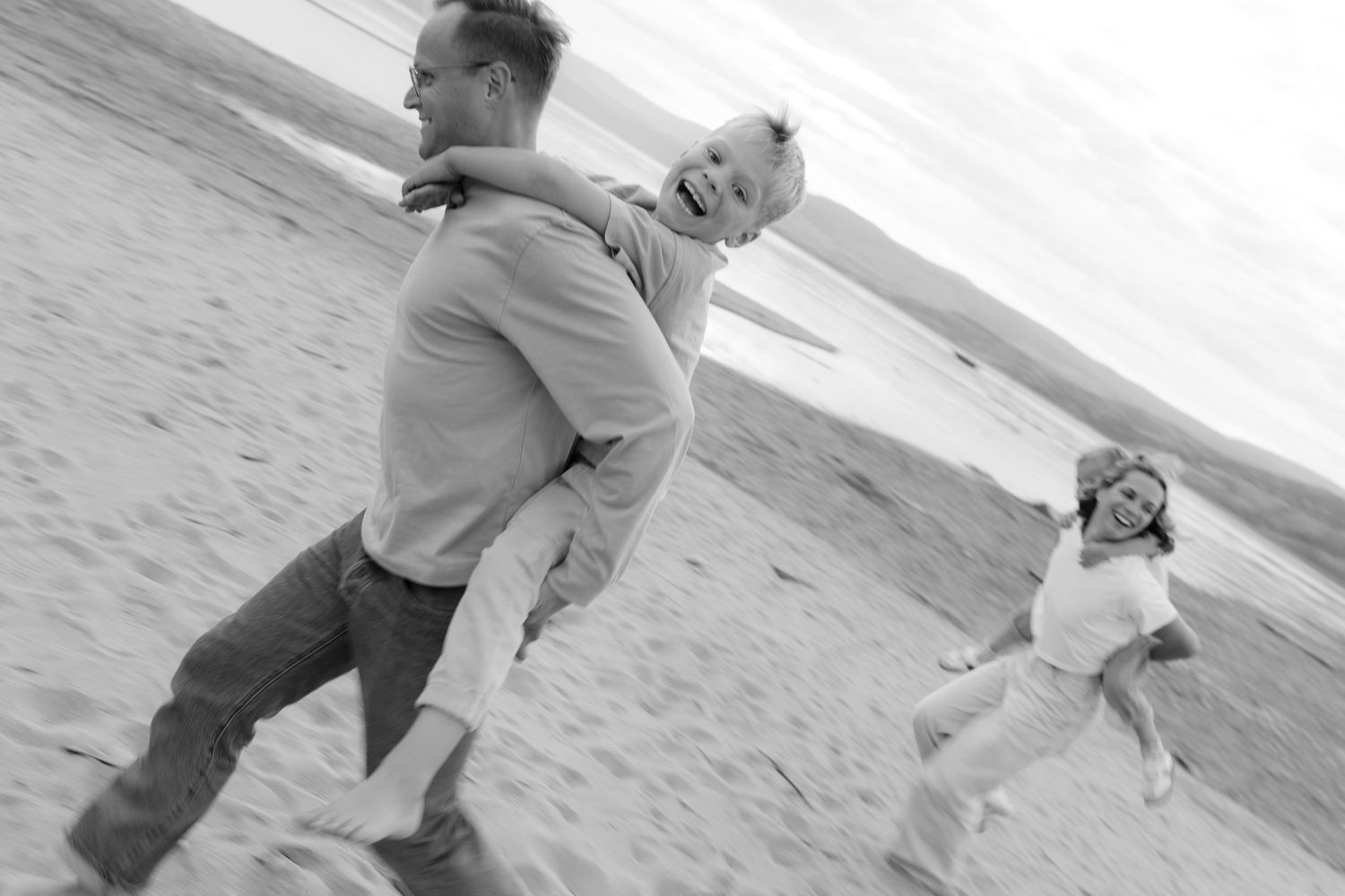 A person in a gray sweater runs and plays on a sandy beach near the ocean.