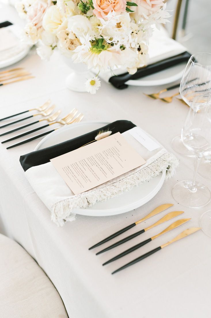 Elegant wedding table setting with white and peach floral centerpiece and gold flatware.