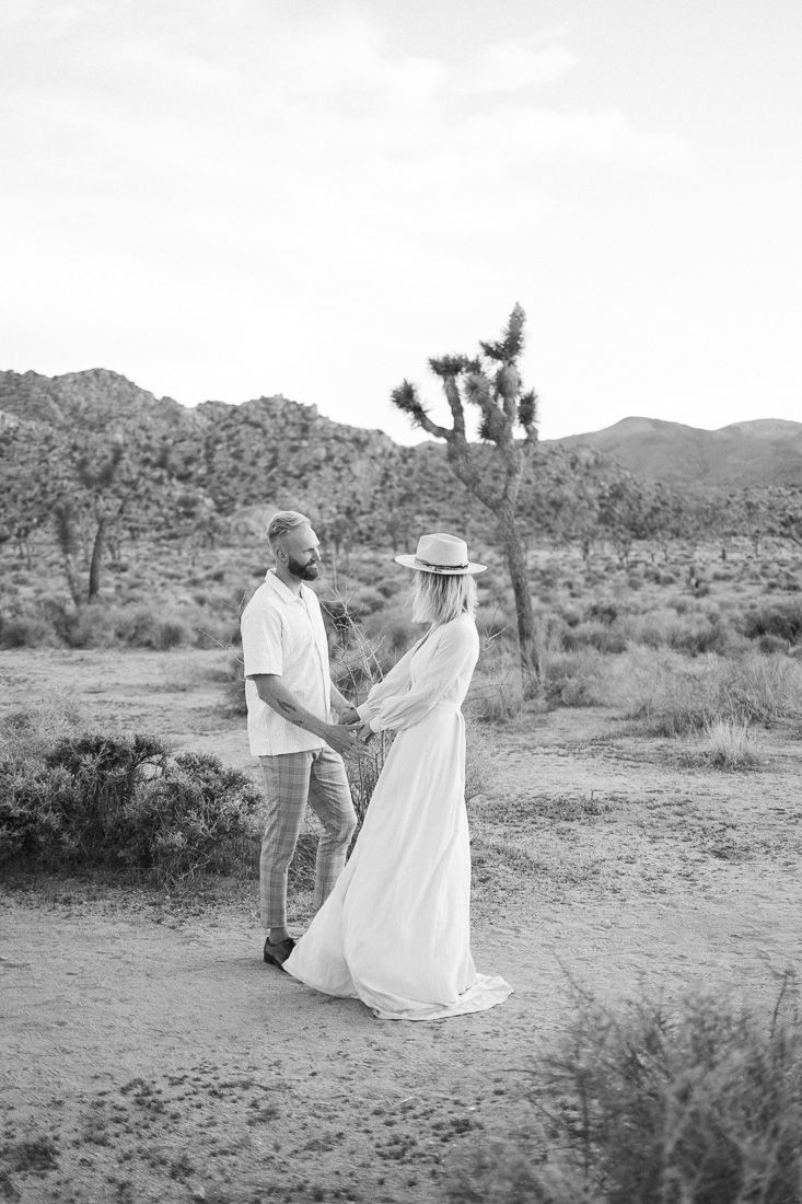 Black and white photo of a couple sharing an intimate moment in a desert setting with mountains behind them.