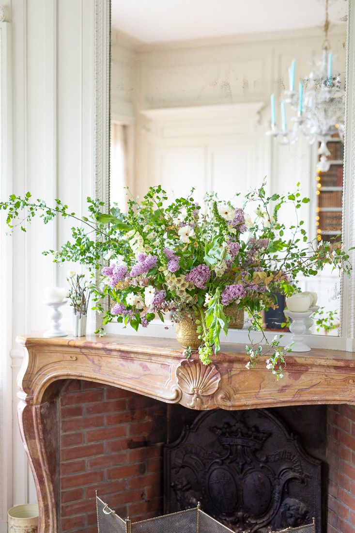 Fresh spring floral arrangement with trailing vines on antique wooden fireplace mantel.
