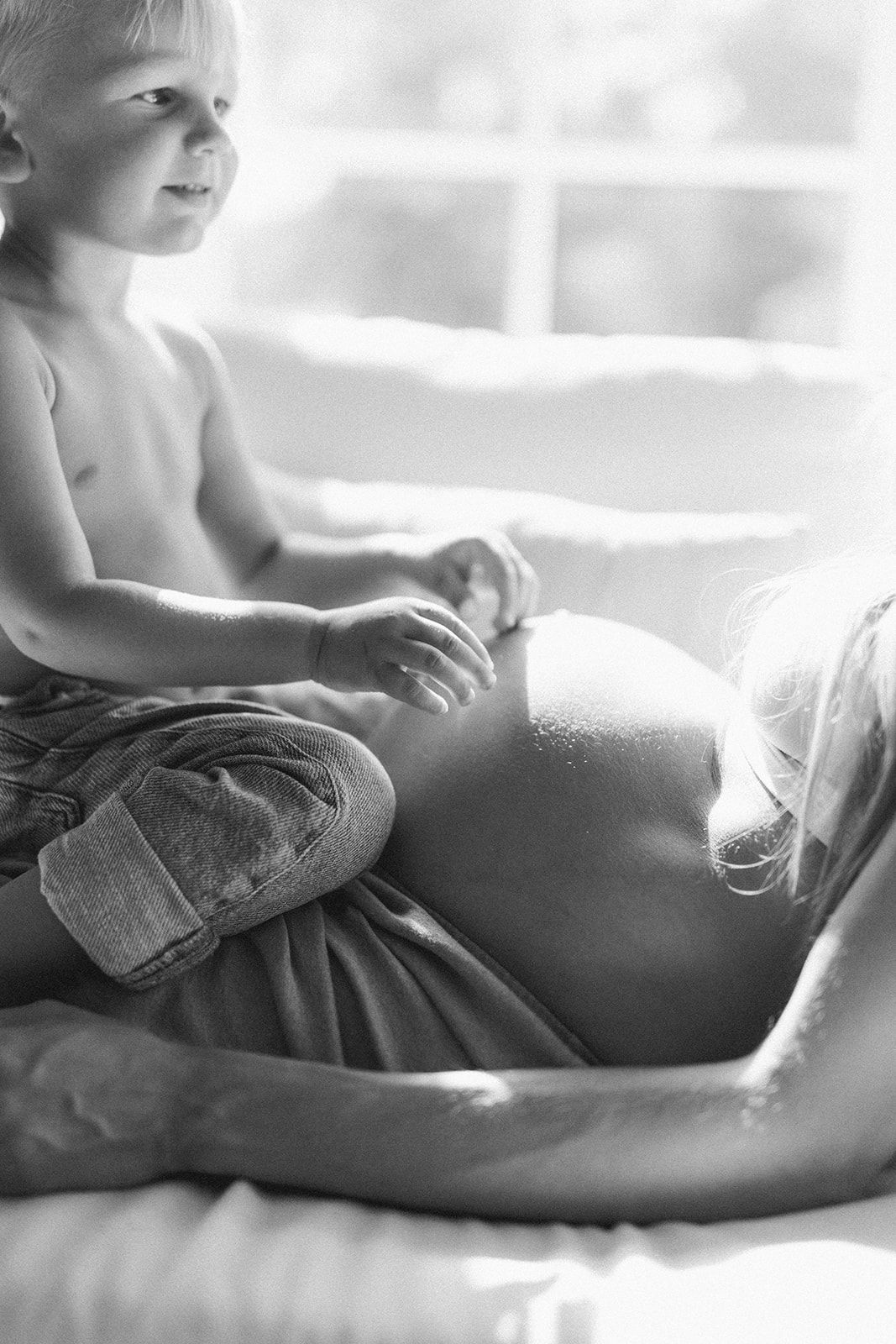 A tender black and white intimate portrait of parent and child sharing a quiet moment in soft window light.