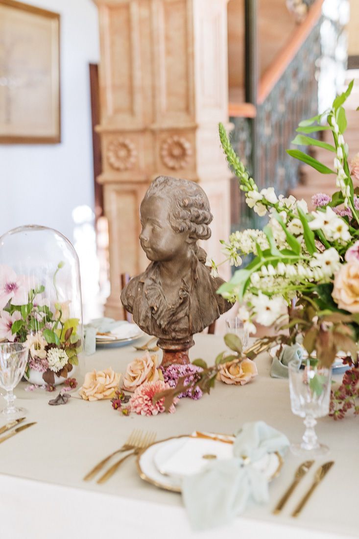 Elegant table setting with classical bust sculpture and delicate floral arrangements in romantic vintage style.