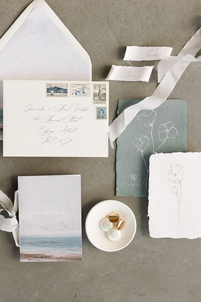 Elegant wedding invitation suite with beach motif and delicate floral illustrations on gray background.