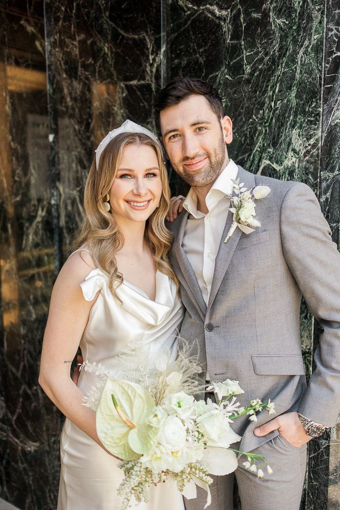 Wedding portrait with elegant white bouquet against green marble wall.