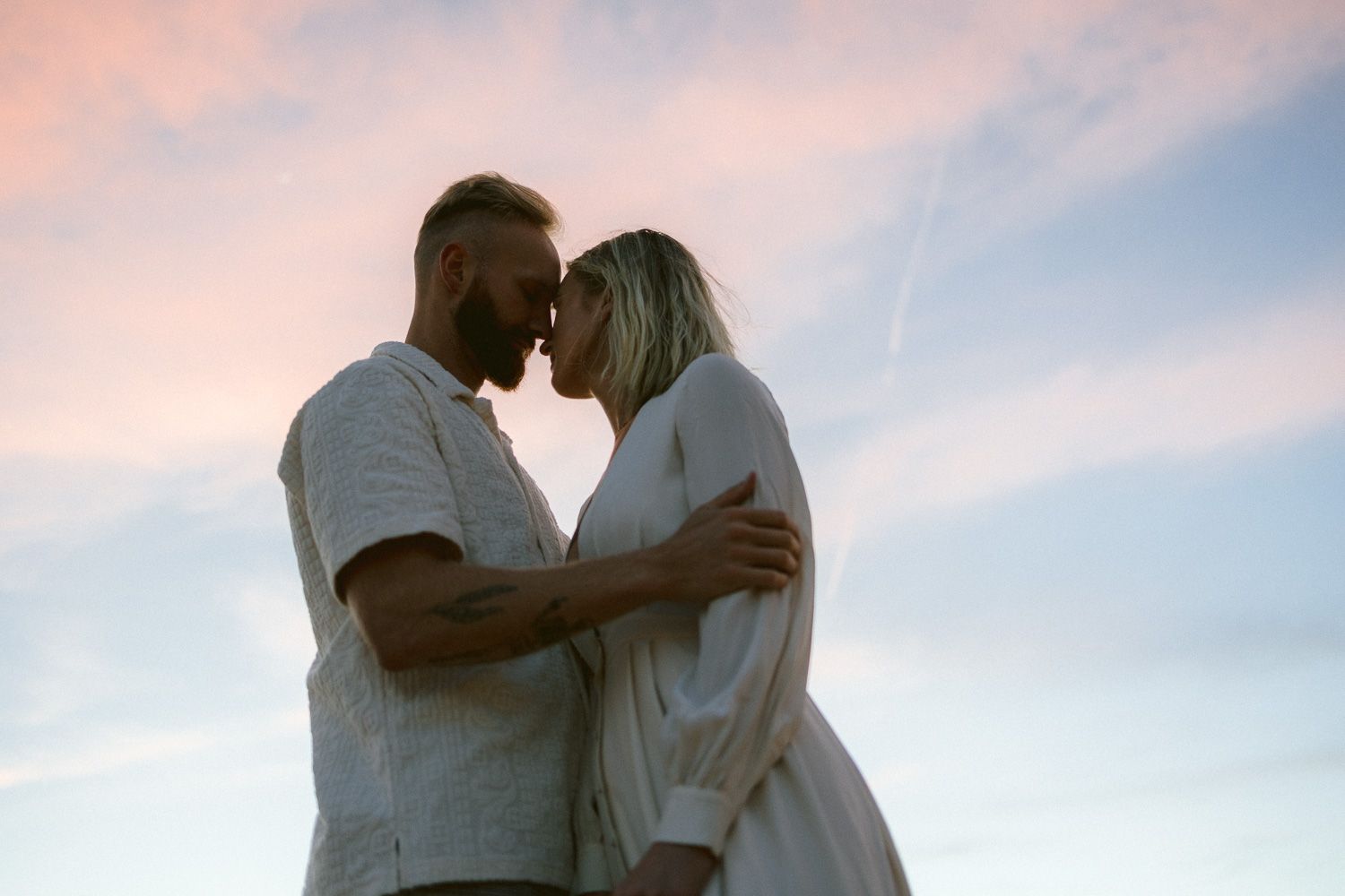 A couple shares an intimate moment silhouetted against a pastel sunset sky.