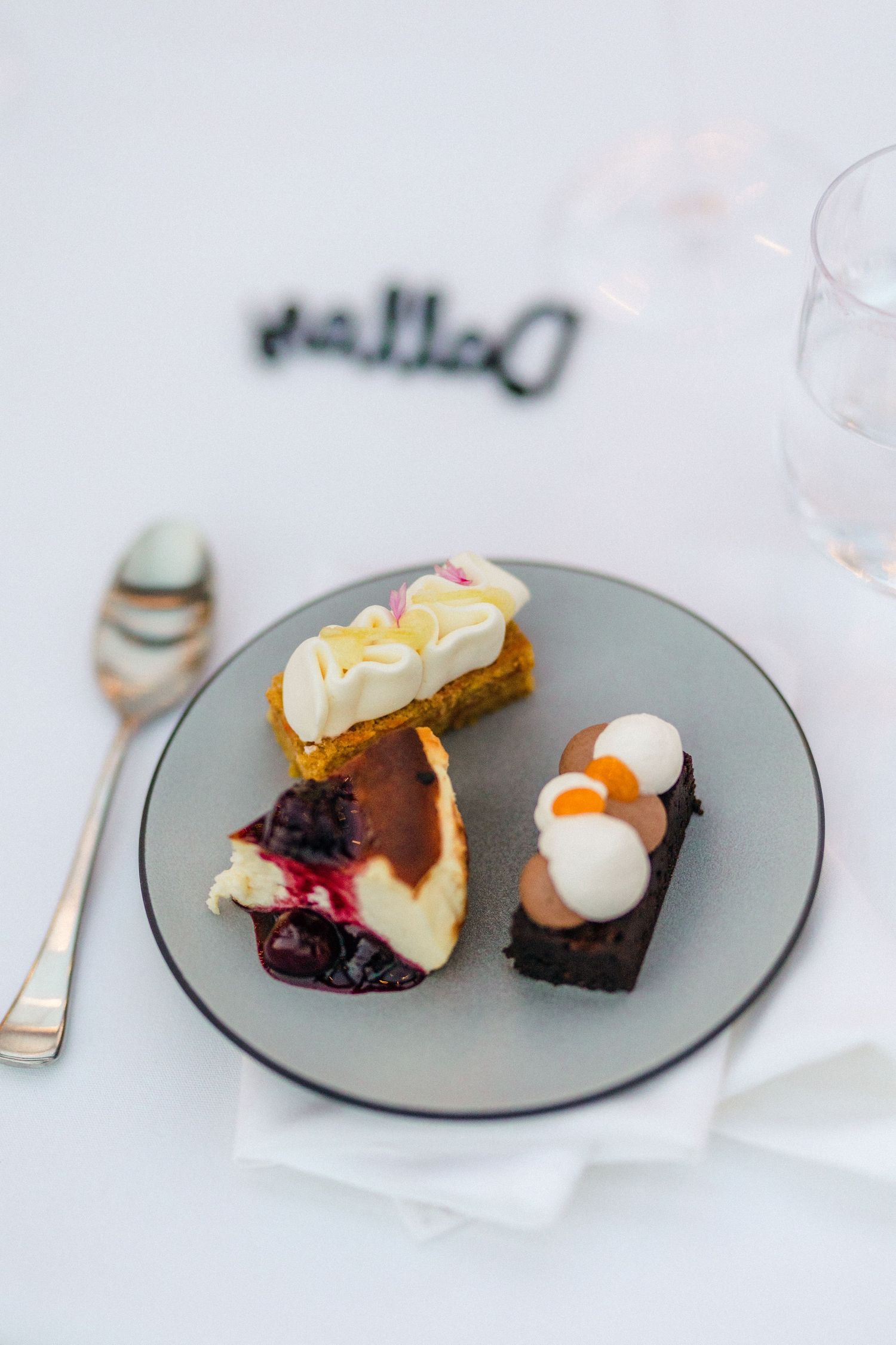 Four gray plates displaying assorted elegant desserts with cream, berries and garnishes on a white tablecloth.