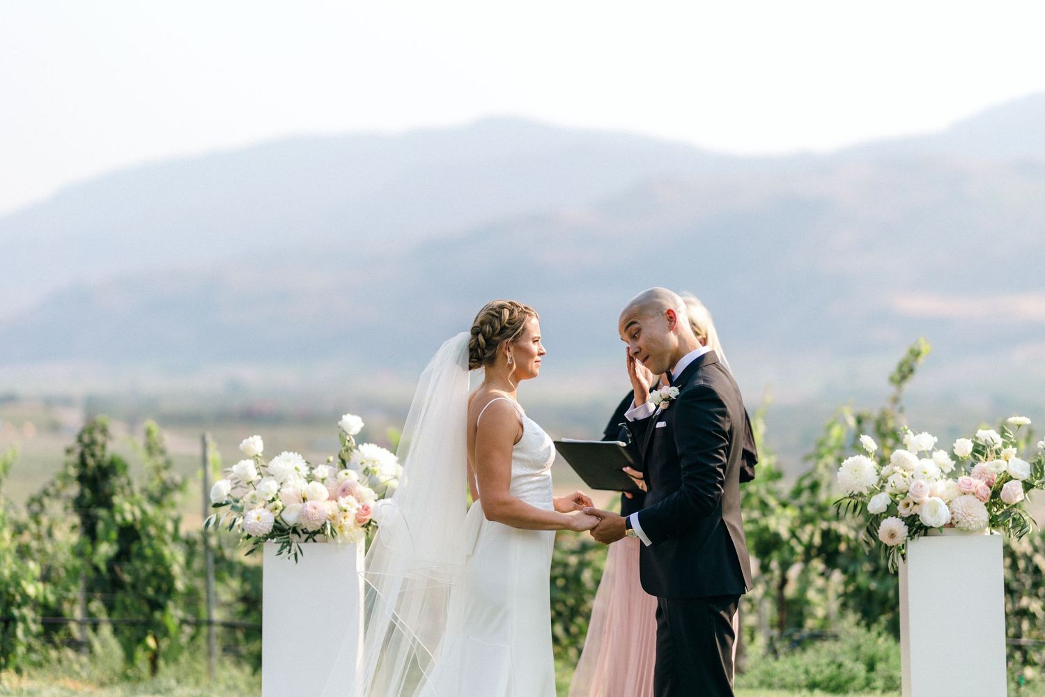 Couple sharing an intimate moment in a vineyard with mountains in the background.