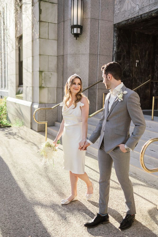 Sunlit wedding portrait outside classic stone building with brass railings.