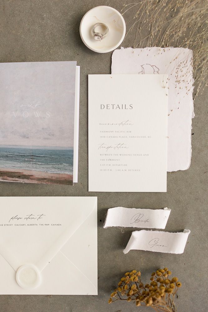 Wedding stationery flat lay featuring details card, beach artwork, and dried flowers.
