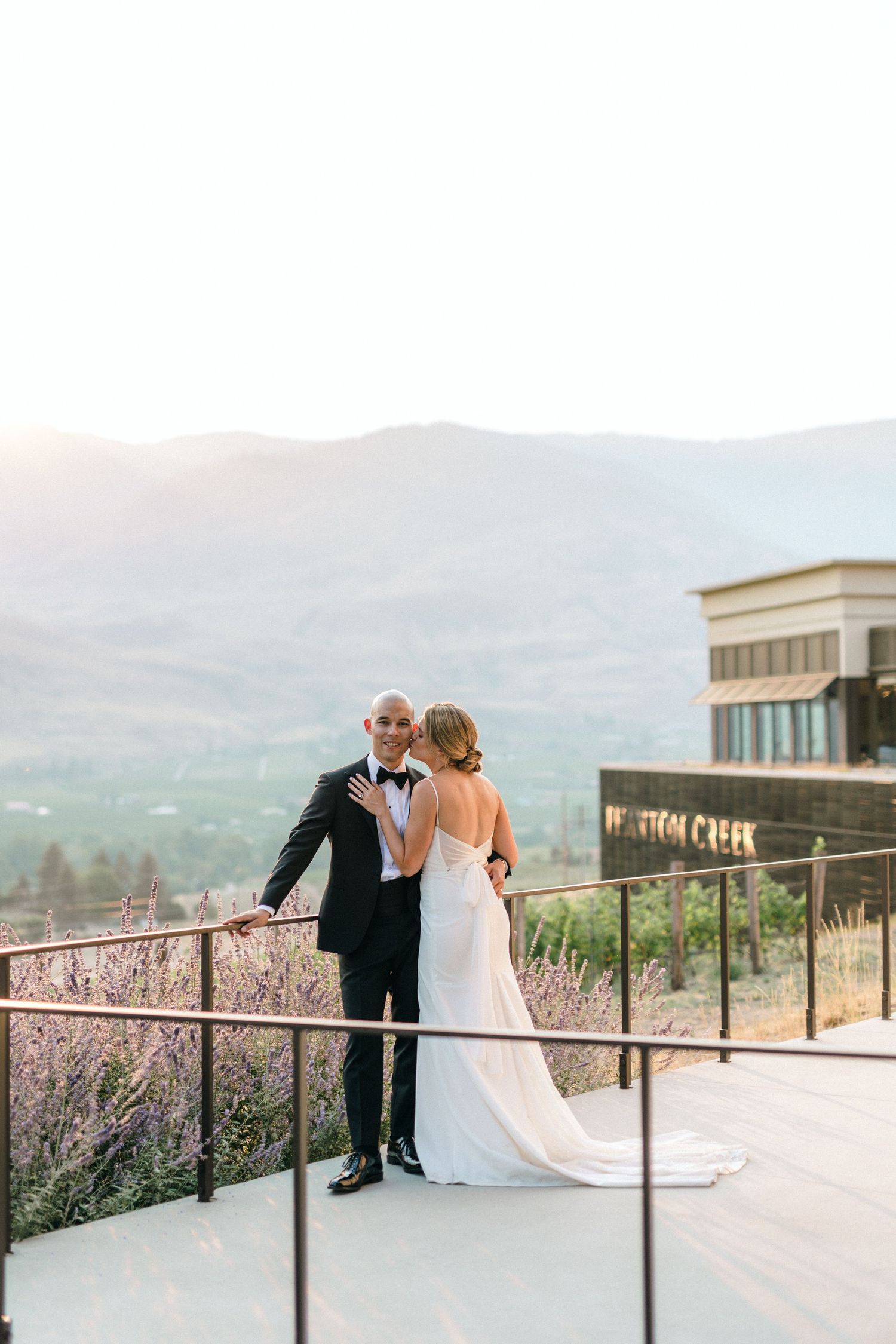 A couple shares a romantic moment on a scenic mountain terrace overlooking a misty valley at sunset.