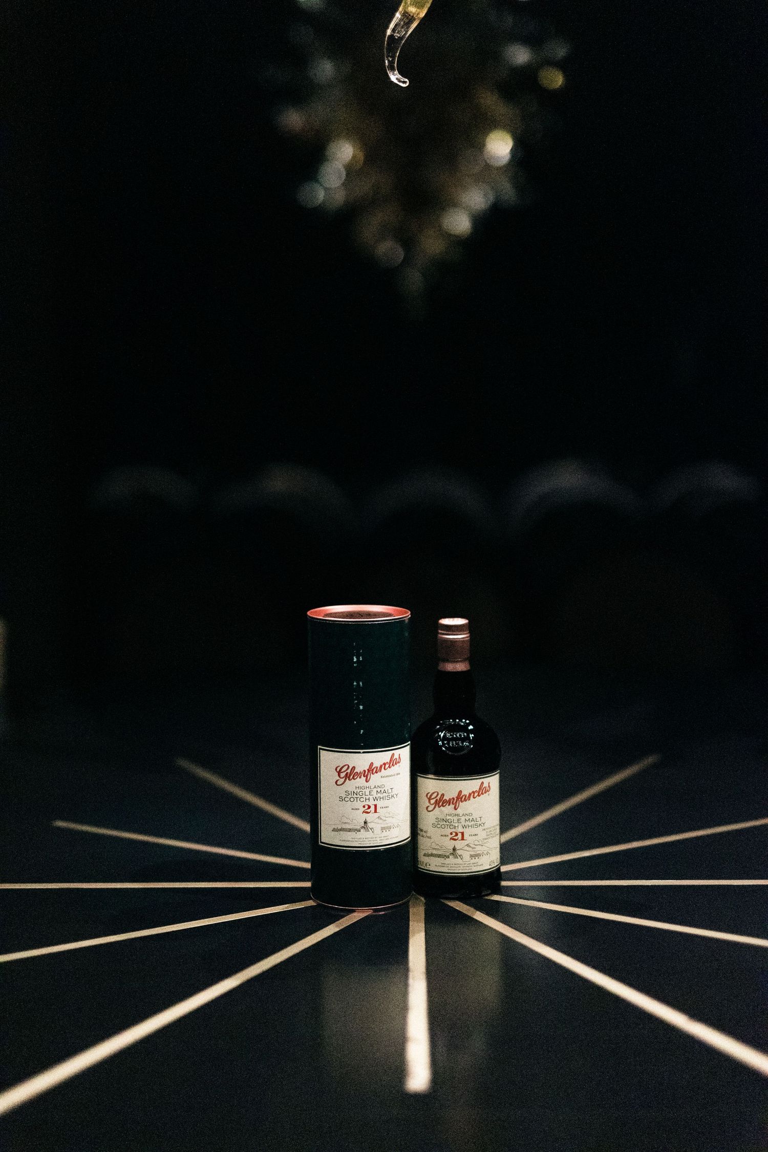Two wine bottles arranged artistically on a dark surface with radiating lines creating a dramatic lighting effect.