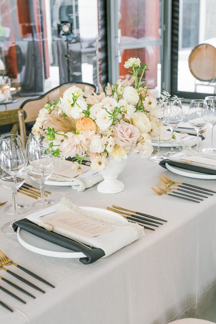 Elegant table setting with blush and white floral centerpiece, gold flatware, and crystal glassware.