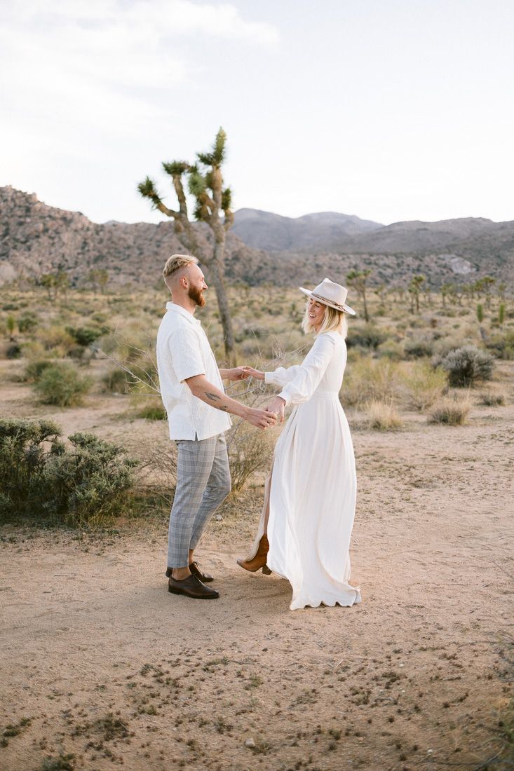 Desert engagement photo with couple in white outfits standing among Joshua trees.