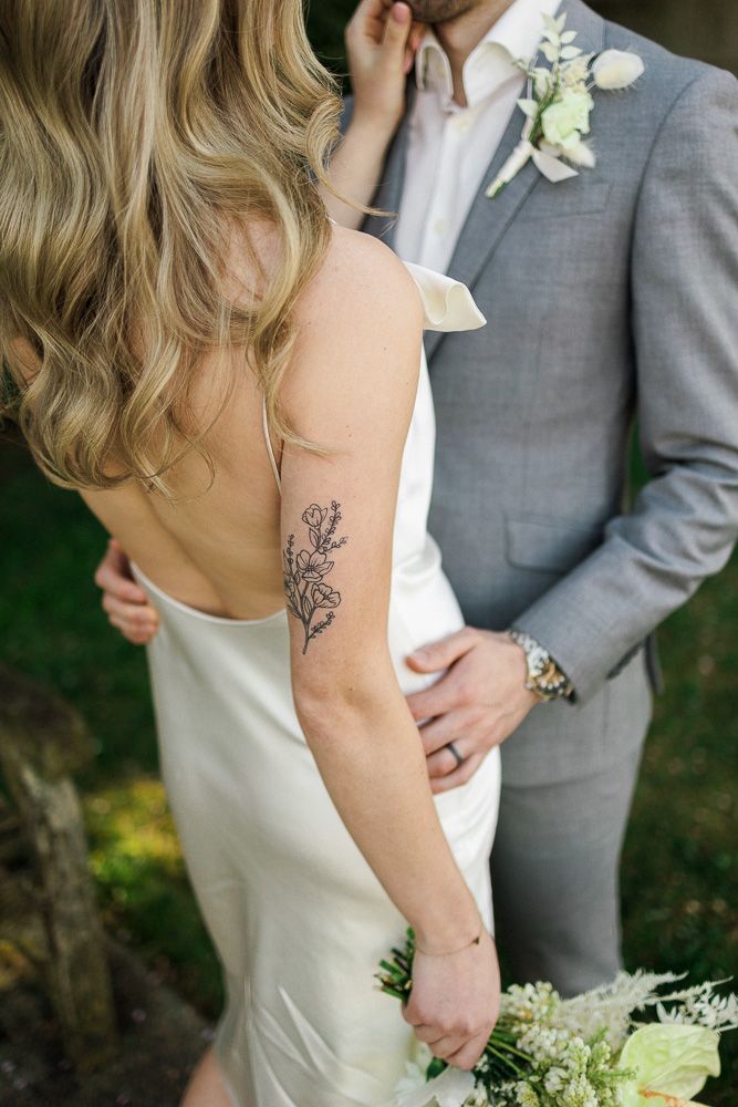 Elegant floral tattoo detail on bride's arm with grey suited groom and boutonniere.