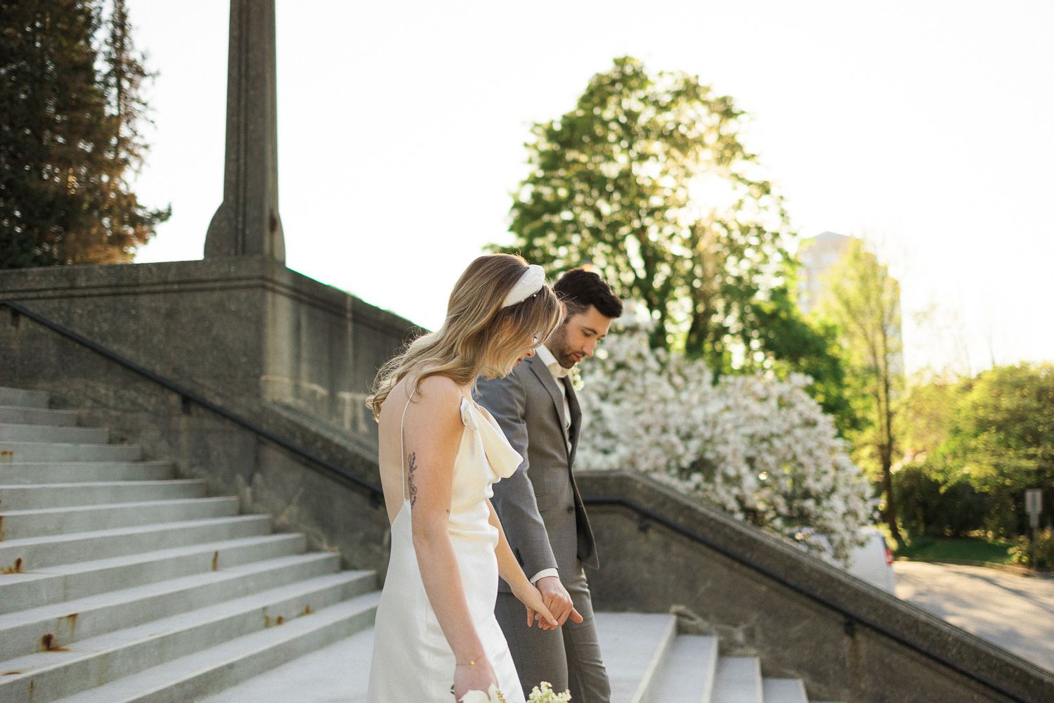 A couple in wedding attire descends stone steps at a historic building during golden hour.