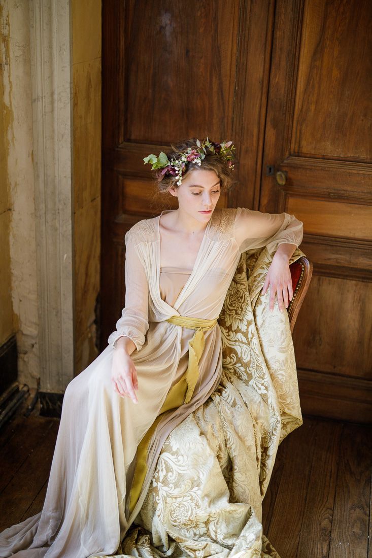 Ethereal bridal portrait with flowing cream gown and floral crown in vintage interior setting.