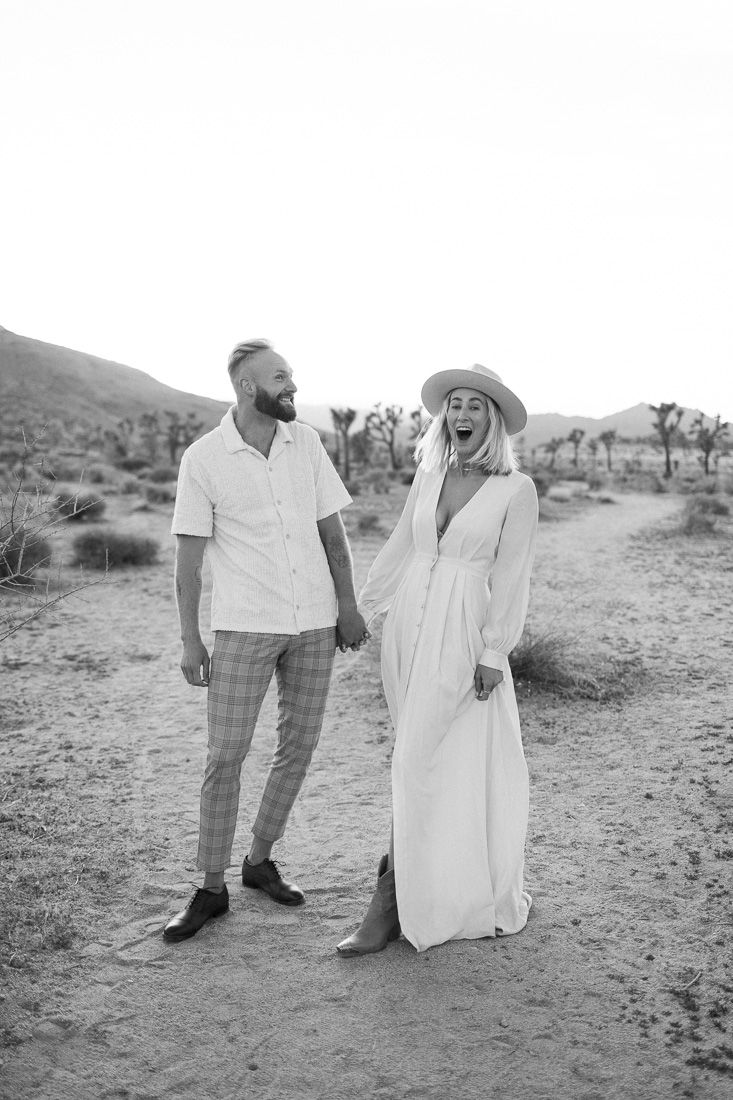A couple shares a joyful moment together in a desert landscape with mountains and Joshua trees in the background.