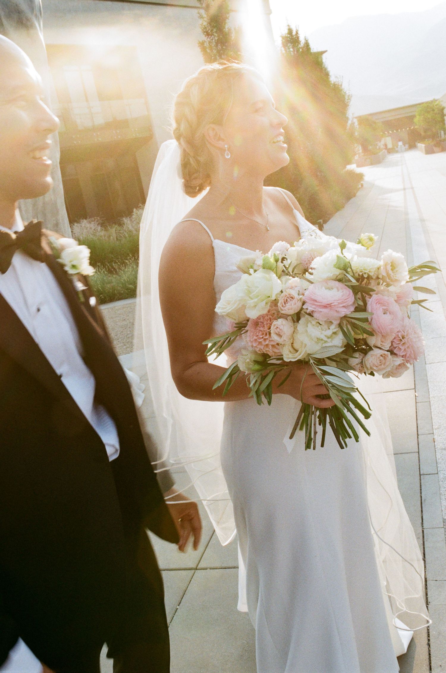 Sun-drenched wedding photo with bride holding pink and white bouquet.