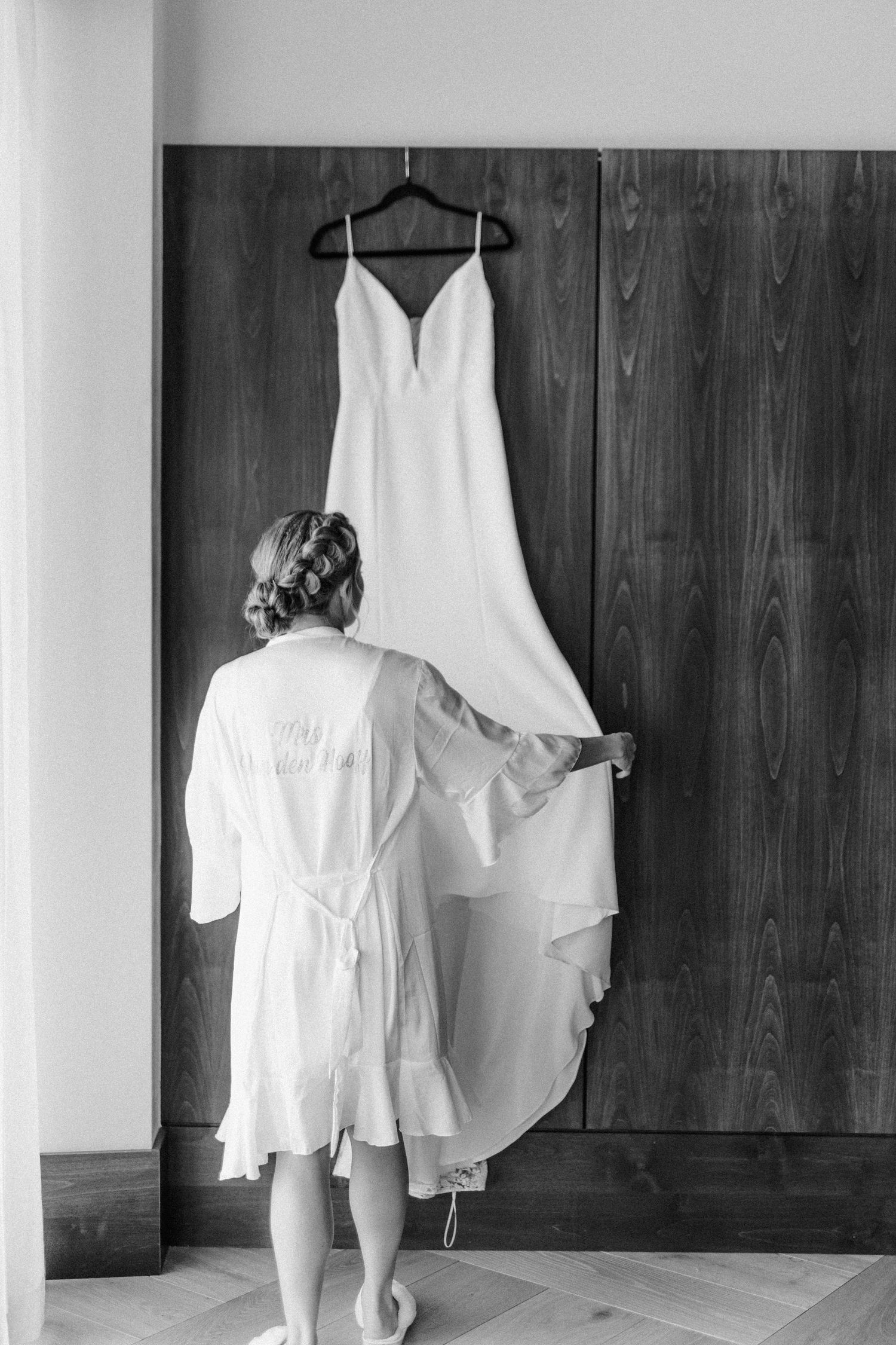 Black and white photos show a child in a white dress approaching a wedding gown hanging on a wooden wall.