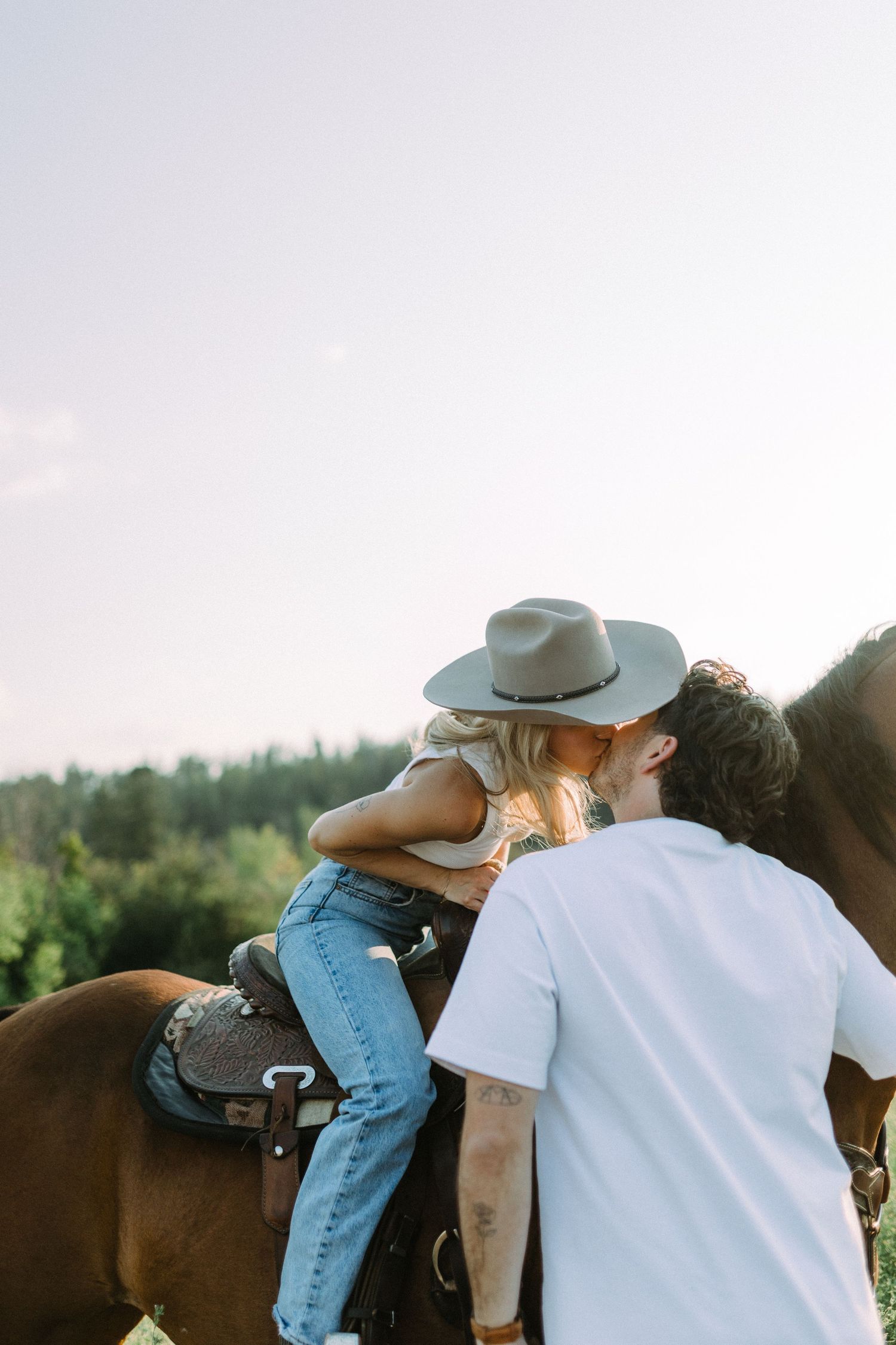 A couple on horseback share a tender moment in a sun-drenched mountain landscape.
