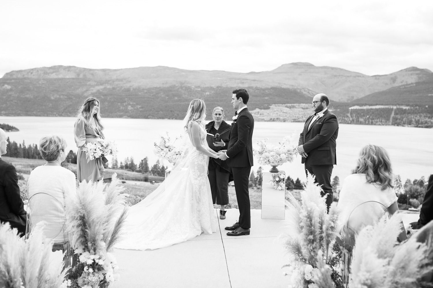 A wedding ceremony takes place on a mountain overlook with dramatic views of lakes and hills.