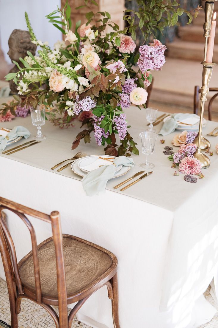 Romantic table setting with lilac and pink floral centerpiece and gold accents.