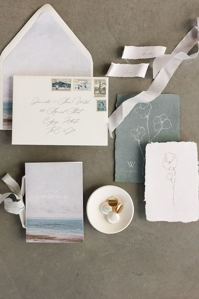 Wedding invitation flat lay with beach artwork, envelopes, and delicate floral designs on gray background.