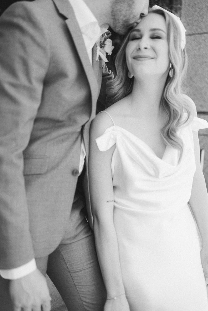 Black and white portrait of couple in formal attire against marble wall.