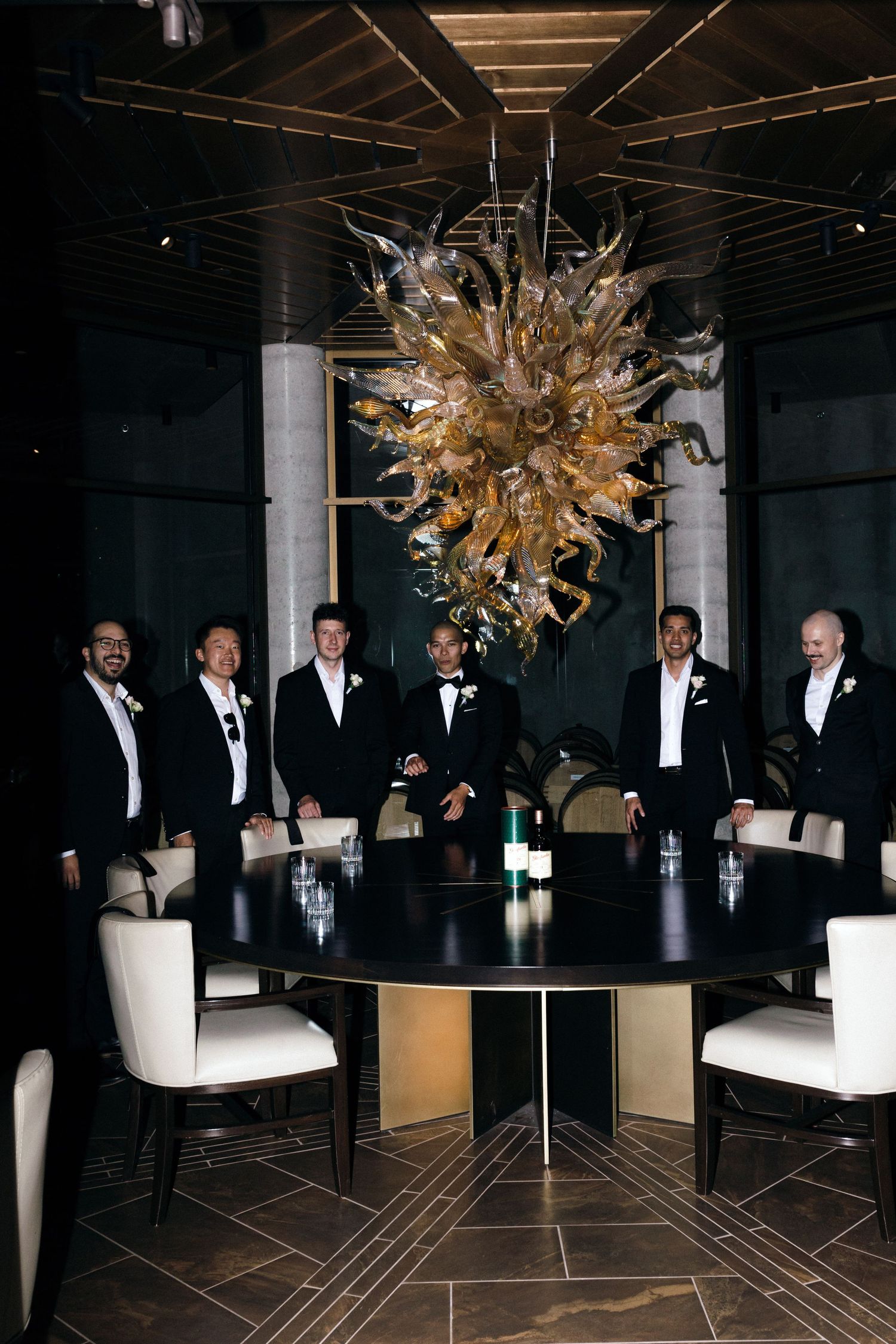 Formal party guests gather beneath an ornate gold chandelier at an elegant table setting.