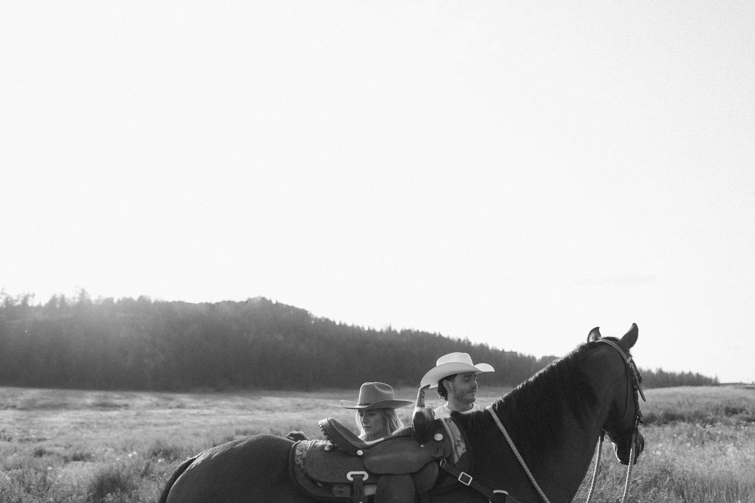 Wide landscape shot of horses and riders on a hillside against a mountain backdrop.