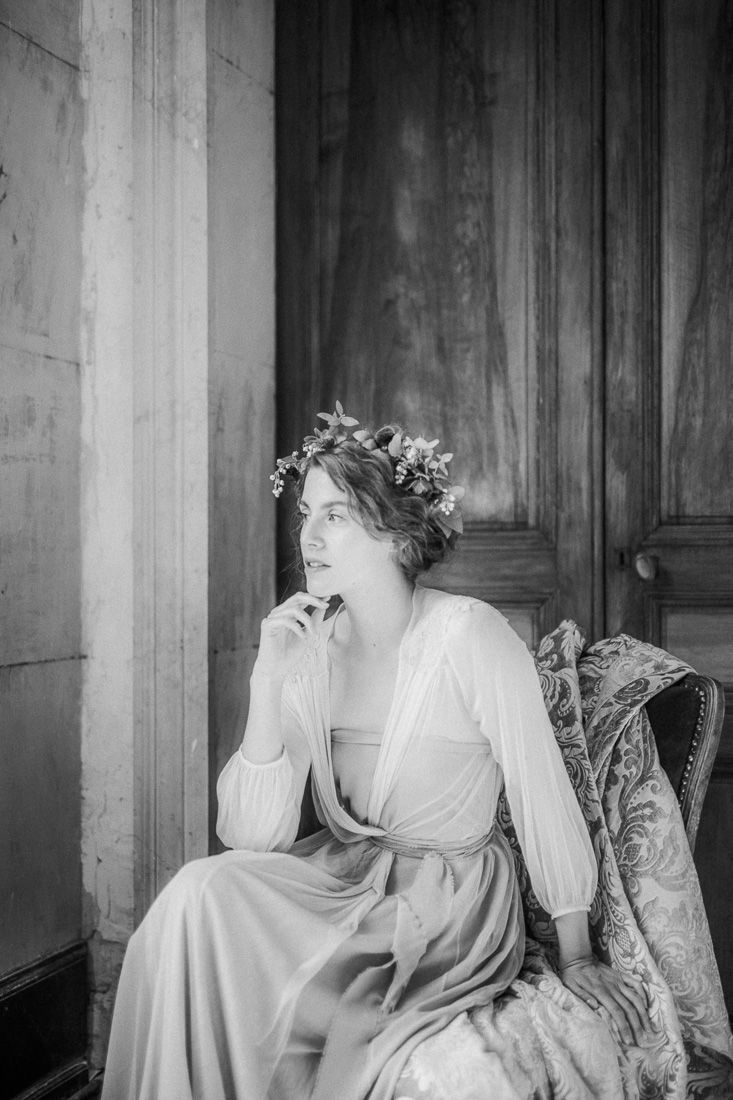 Black and white portrait showing a contemplative pose in a classical setting with floral crown.