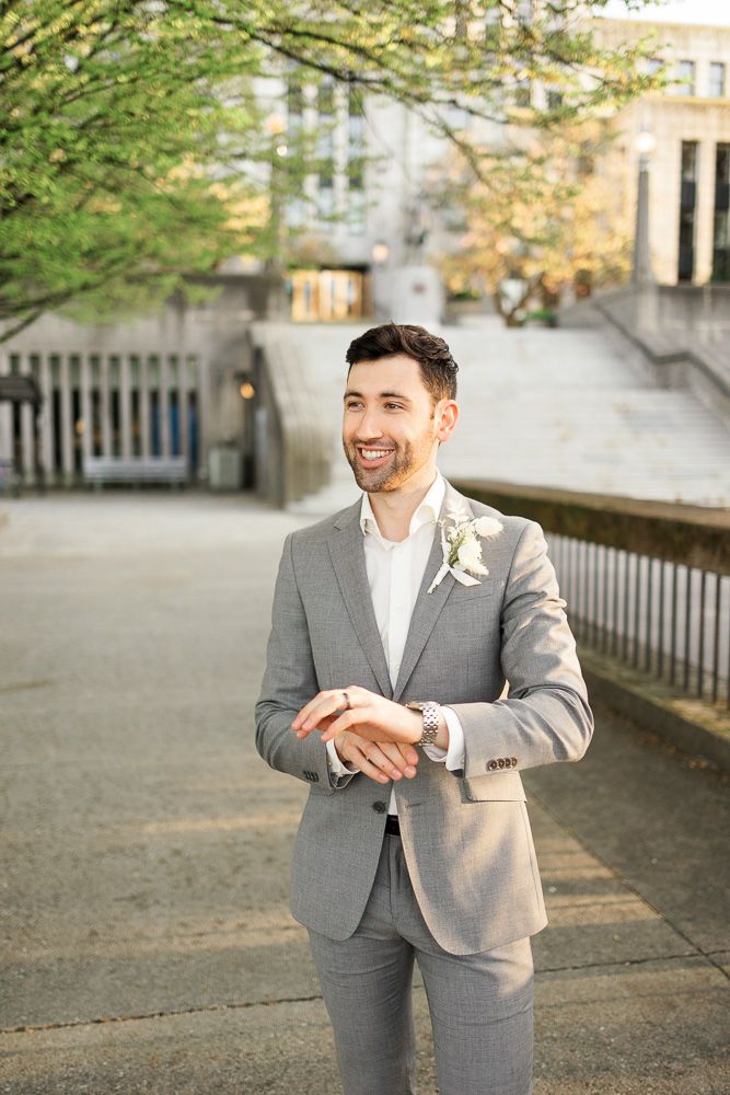 Groom in light gray suit stands outdoors with stone steps in background.