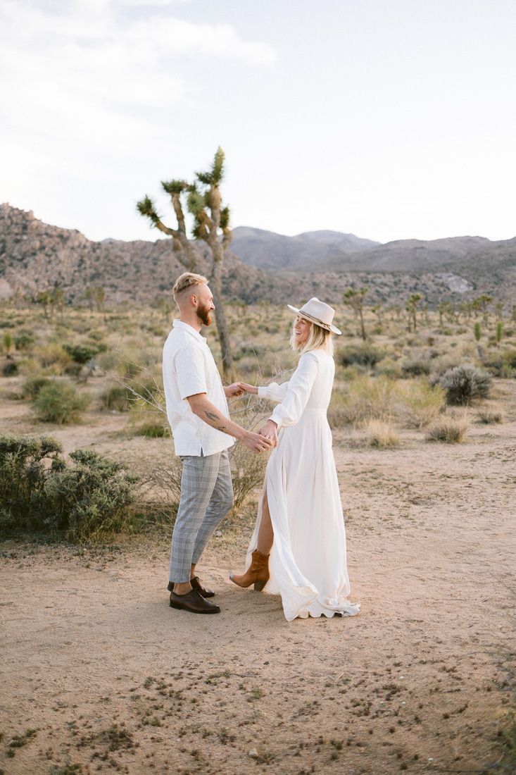 Intimate desert photoshoot featuring a couple in white clothing against a mountainous backdrop.