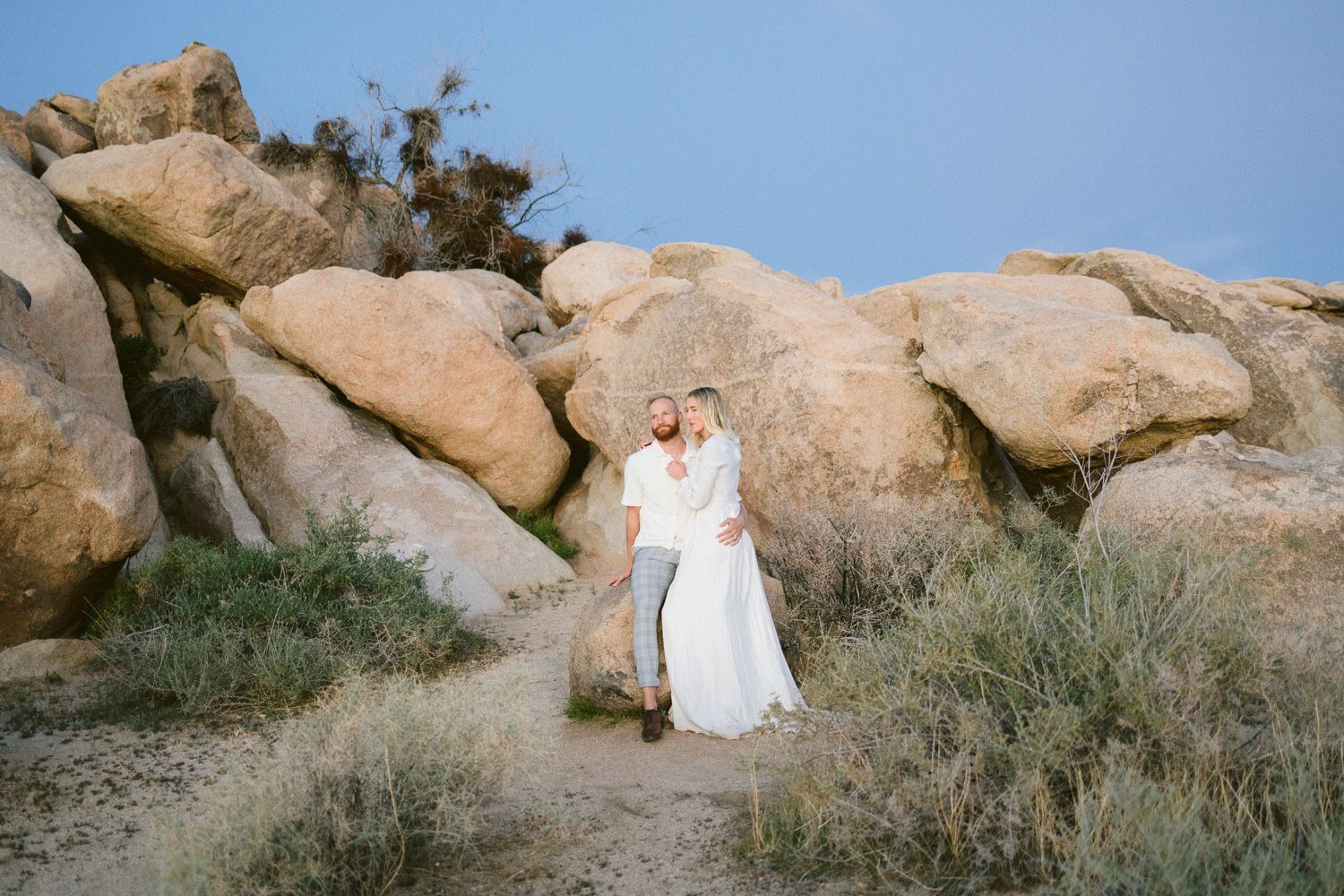 Couple walking hand in hand along desert path surrounded by large rock formations.