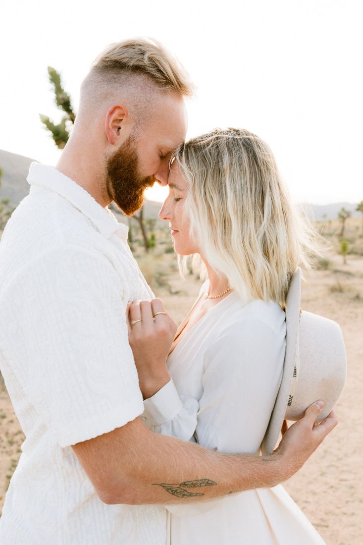 Romantic desert engagement photo of couple in white outfits embracing in Joshua Tree National Park.