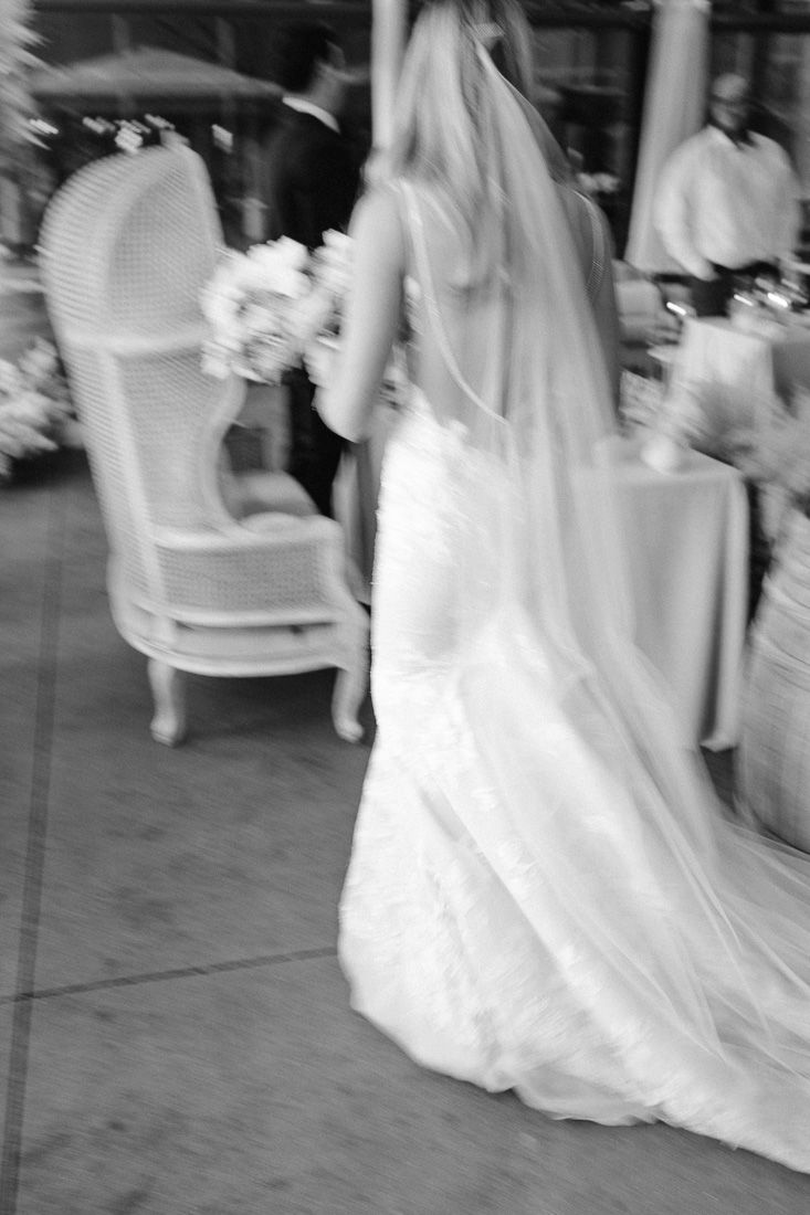A blurred black and white photo of a bride in a flowing white wedding dress holding a bouquet near an elegant chair.