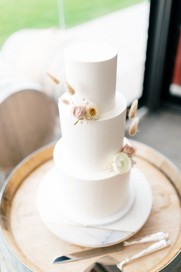 Minimalist three-tier white wedding cake decorated with delicate pink and white roses.