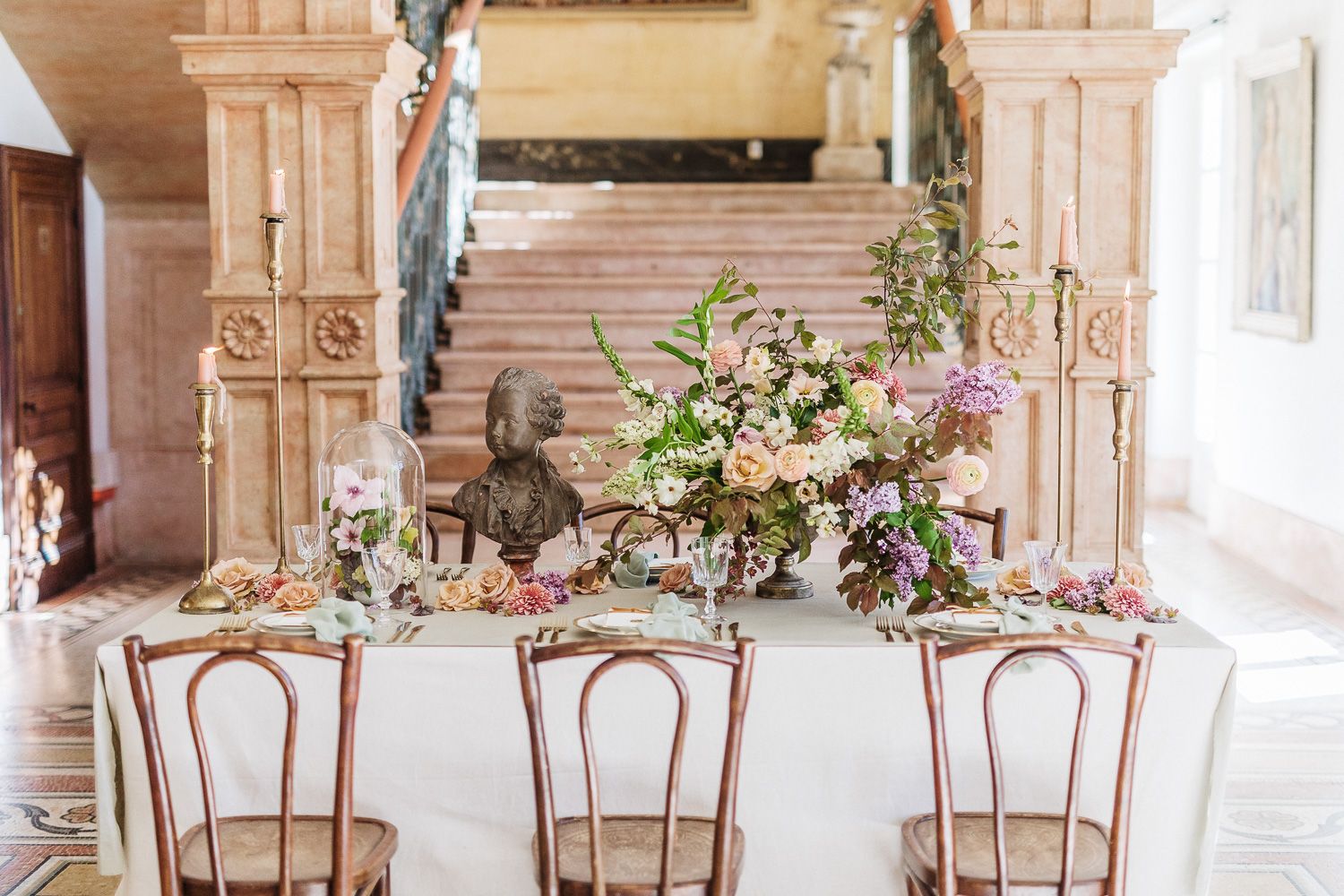 Wedding reception table with vintage bentwood chairs and romantic floral centerpieces in an elegant venue.
