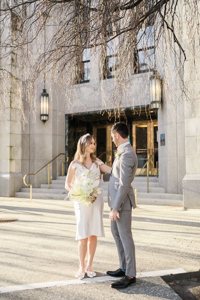 Elegant couple sharing moment outside historic building with hanging branches.