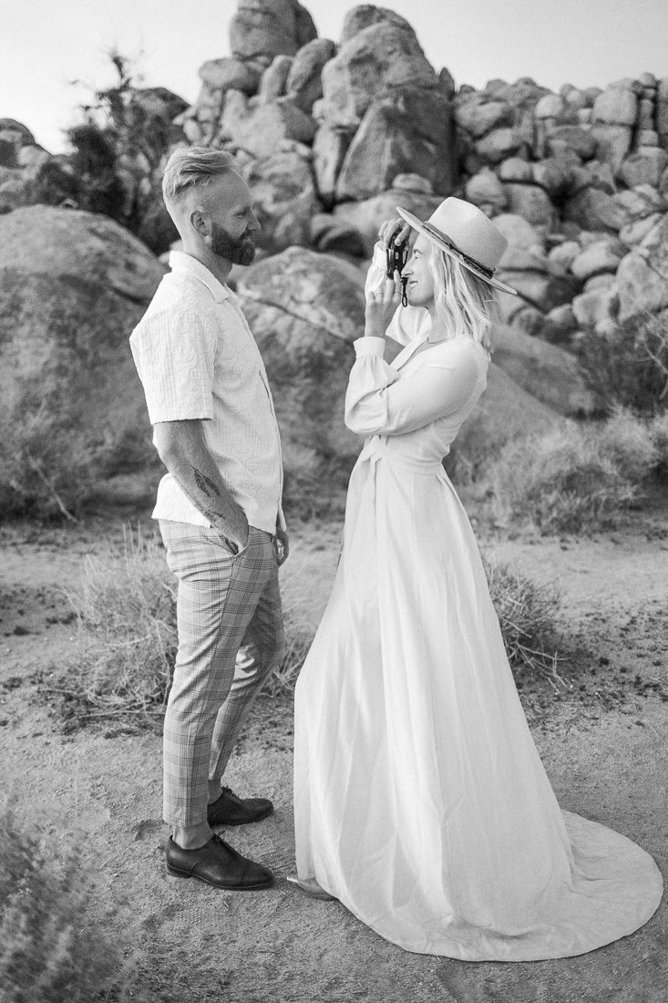 Monochrome portrait of a couple in white and casual attire against desert rocks.