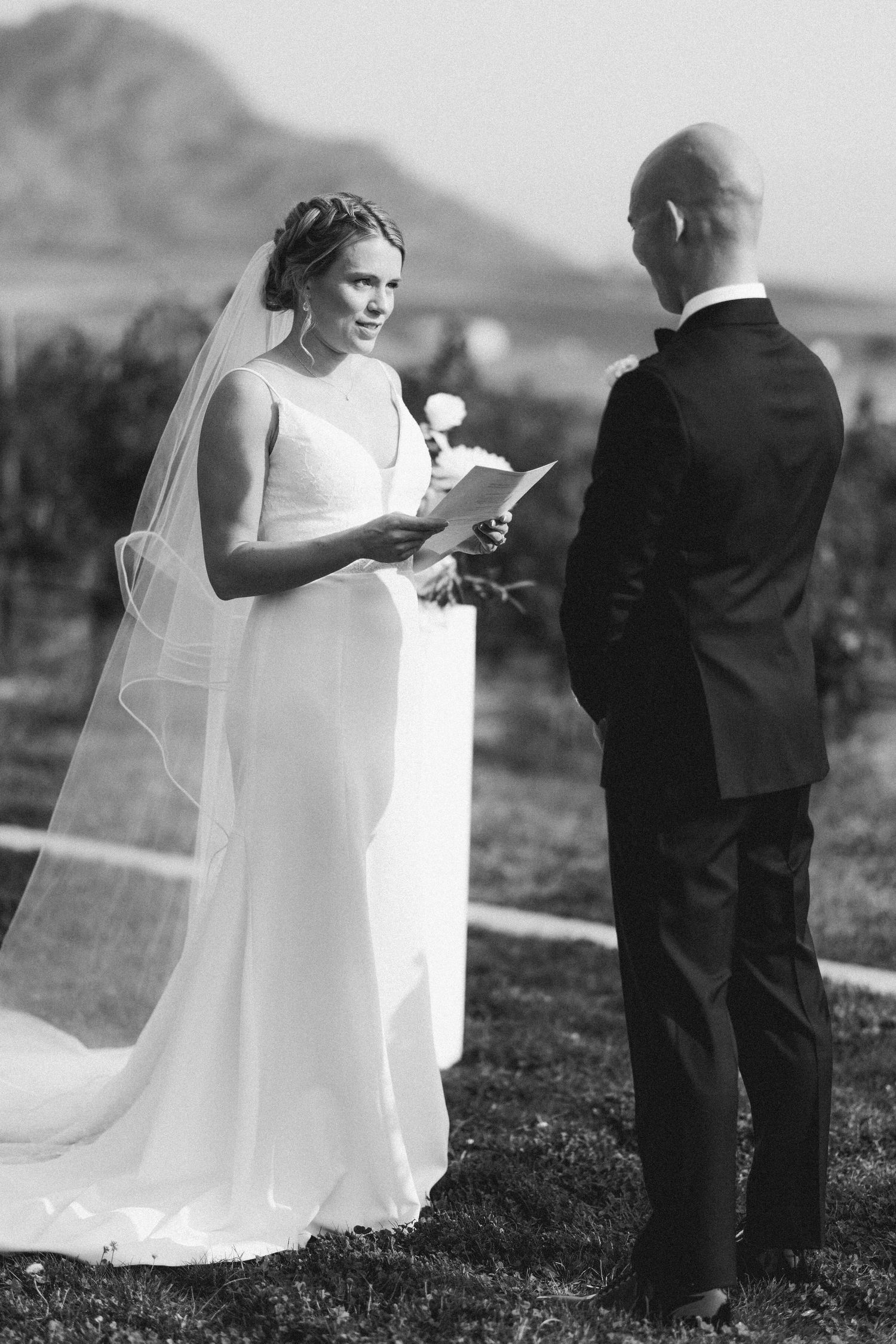 A couple exchanging vows during an outdoor wedding ceremony with mountain backdrop.