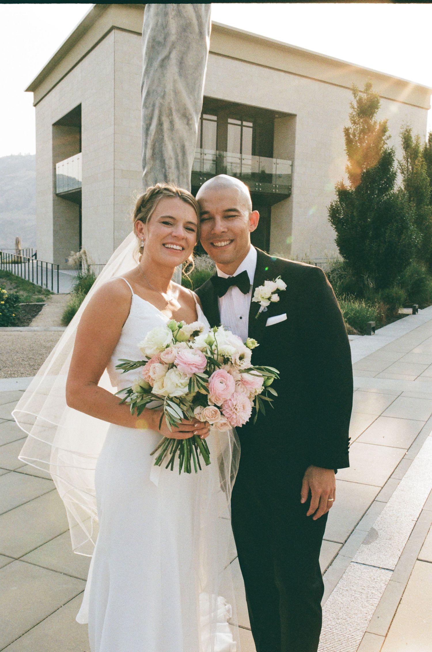 Wedding couple embracing and laughing together outside a modern stone building.