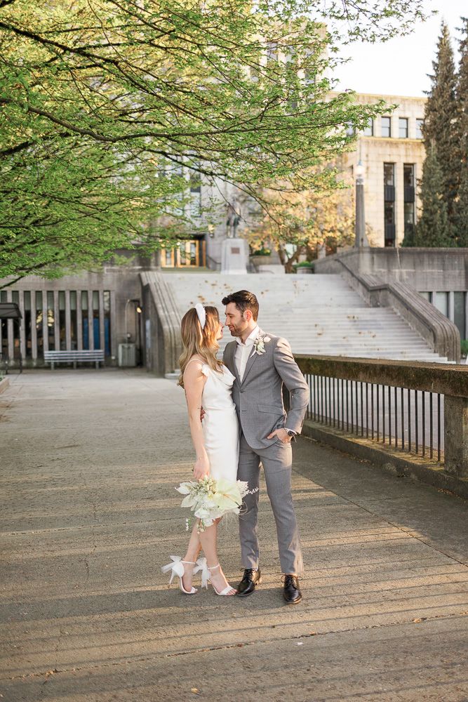 A couple in wedding attire share a romantic moment on a walkway with stone steps in the background.