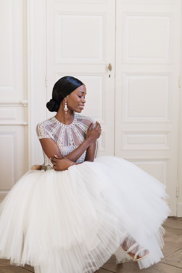 Side view of a bride in a tulle tea-length gown with intricate beaded bodice sitting gracefully.