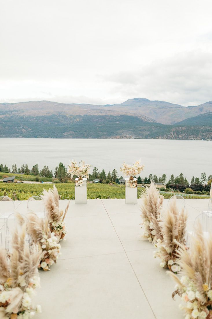 Wedding ceremony aisle lined with pampas grass overlooking a mountain lake landscape.