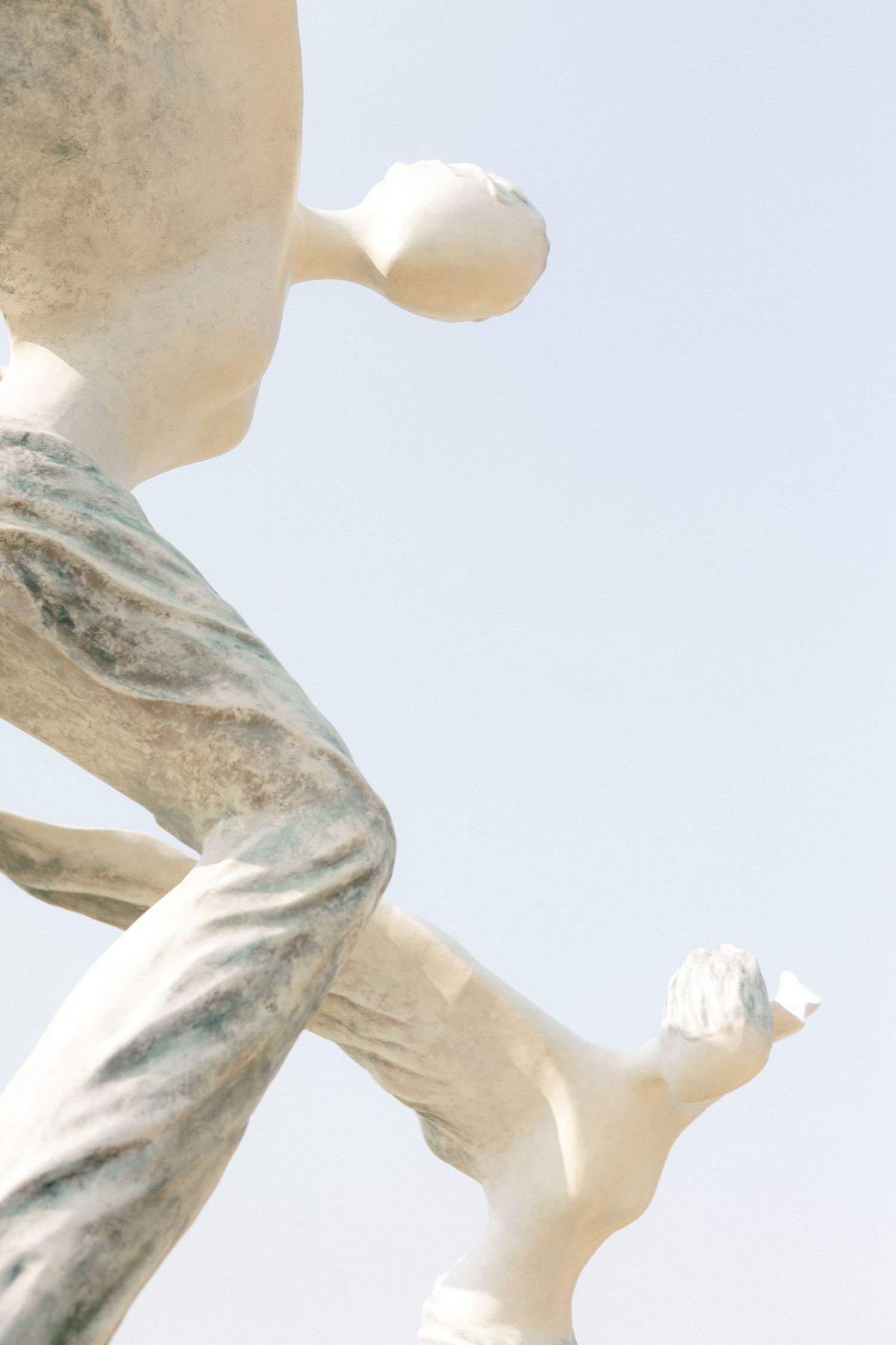 Abstract close-up of white marble statues against a light blue sky.