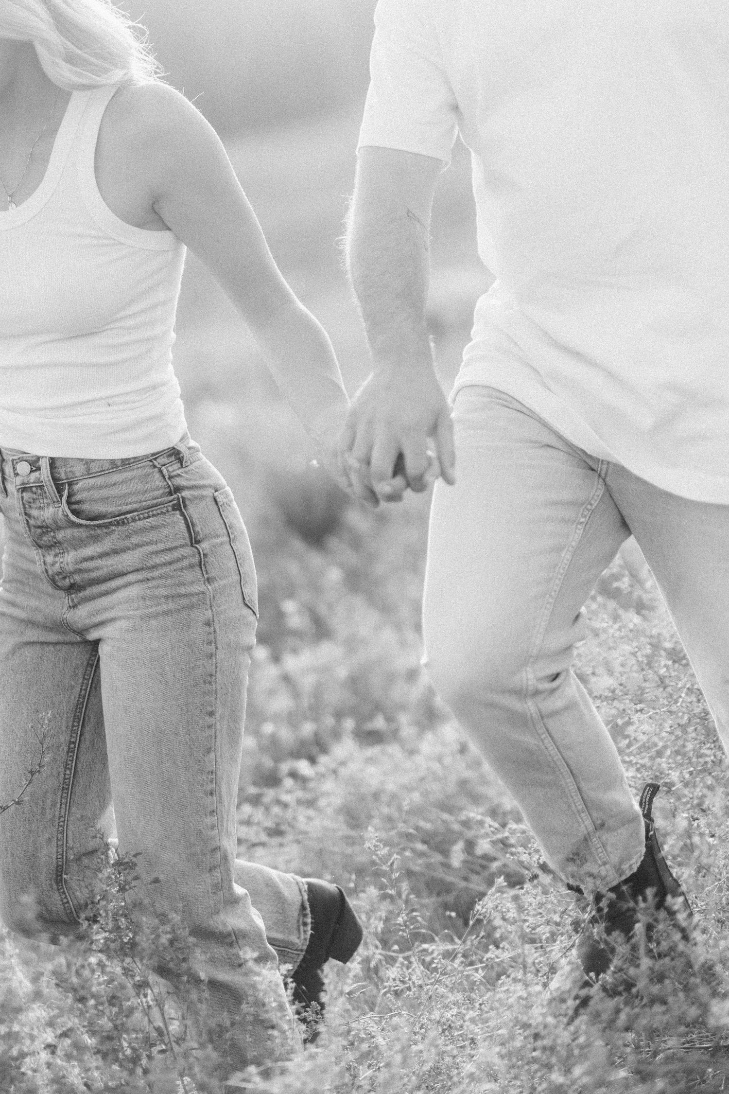 Close-up of two people holding hands while walking through wildflowers in black and white.